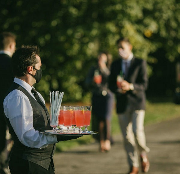 Masked cater waiter tray of cocktails