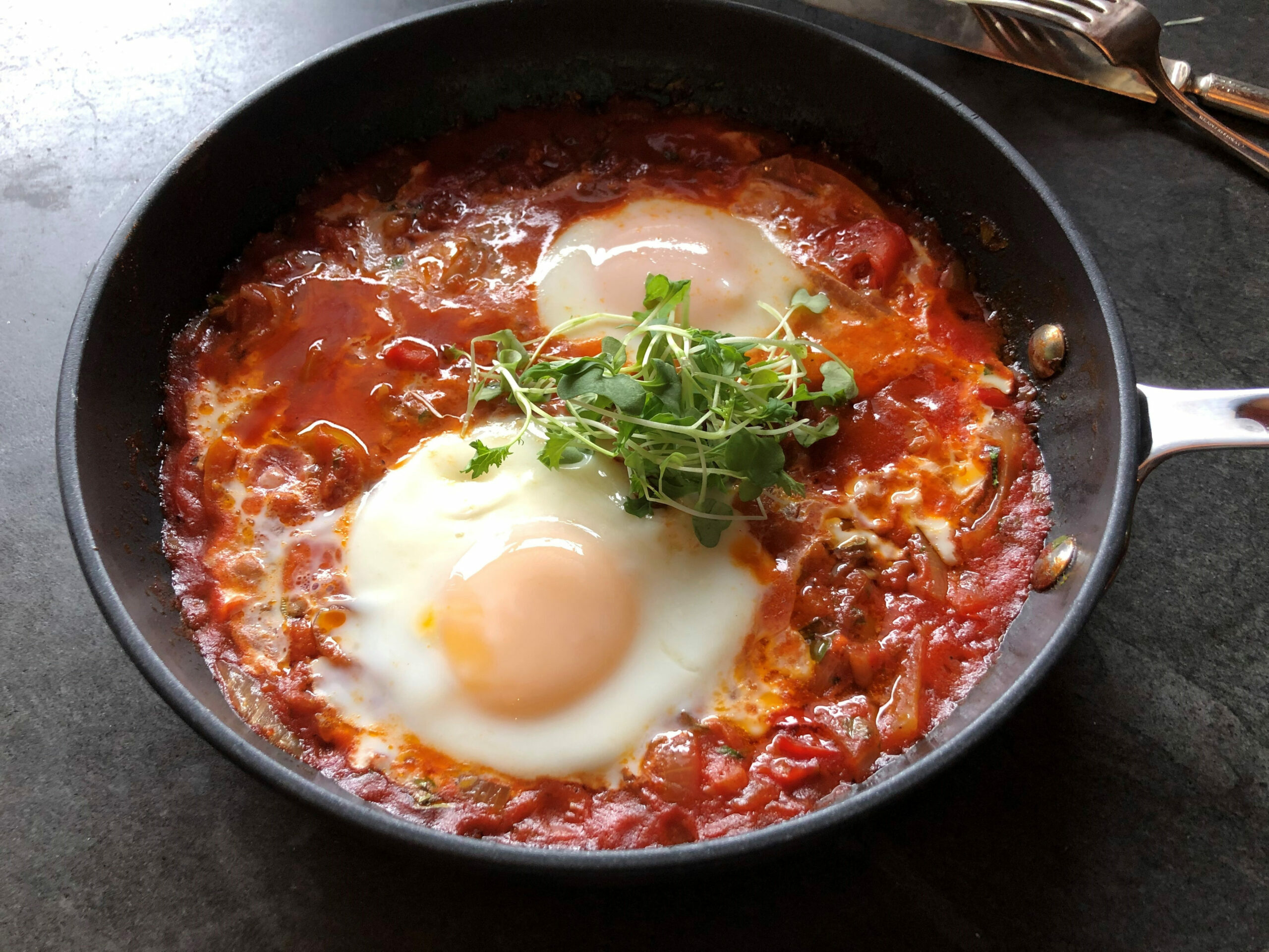 Two eggs nestled in a tomato based sauce in a skillet garnished with greens